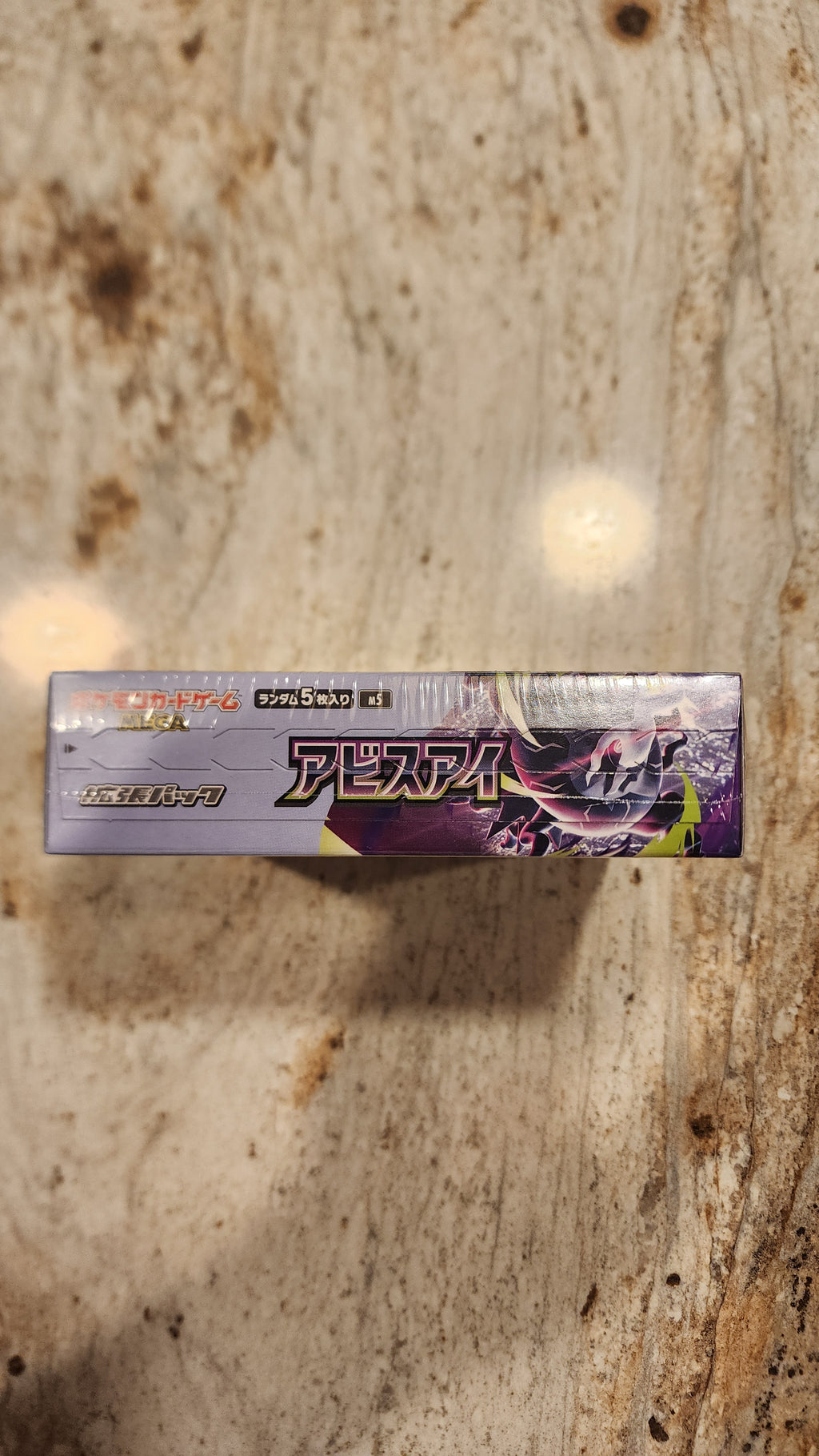 A sealed Japanese Pokémon Tens card pack standing vertically on a textured stone surface.