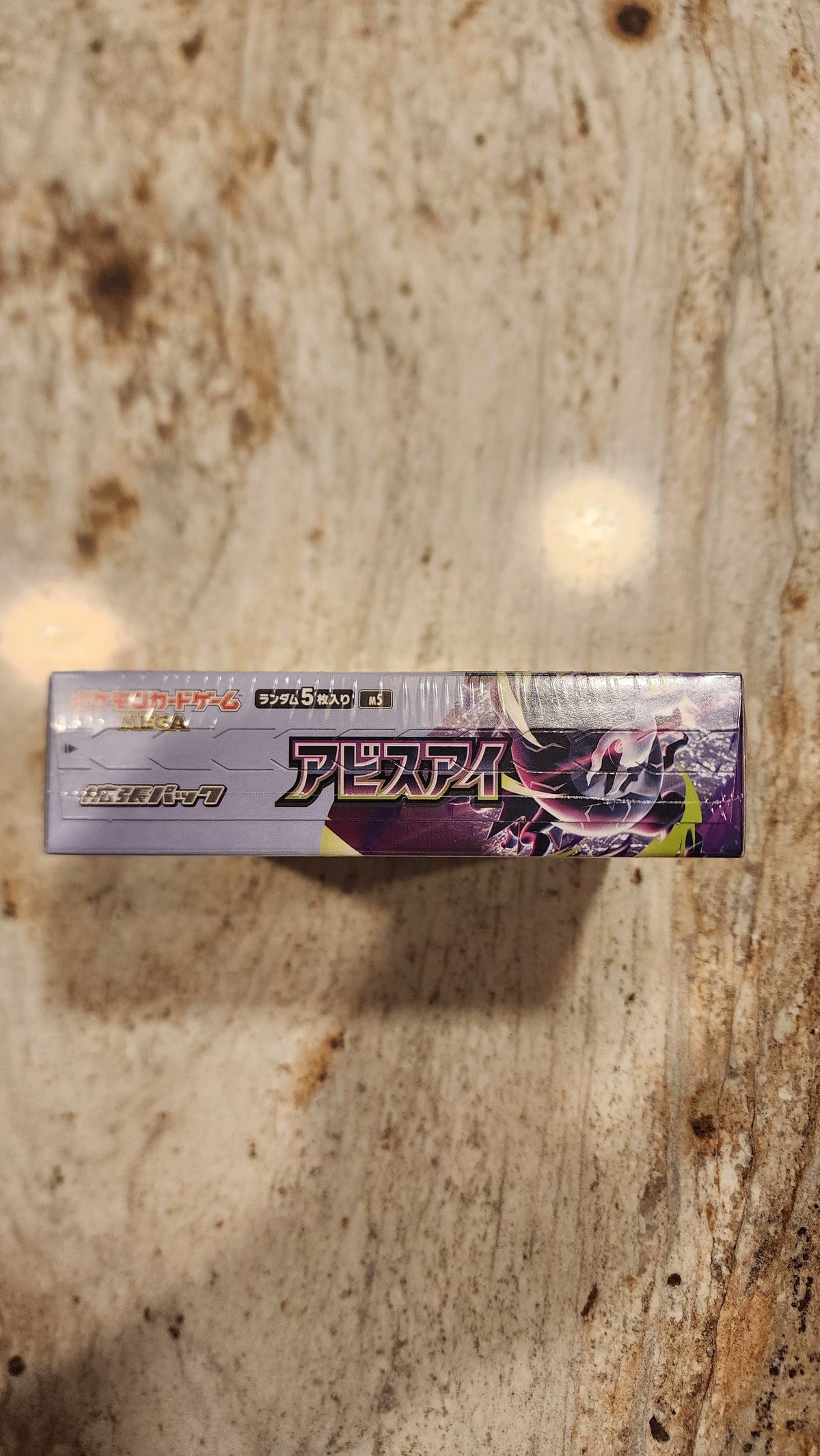 A sealed Japanese Pokémon Tens card pack standing vertically on a textured stone surface.