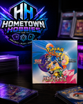 A boxed Pokémon TCG booster pack displayed on a dark tabletop, with several cards fanned out in front and a large Hometown Hobbies LLC logo graphic behind it.