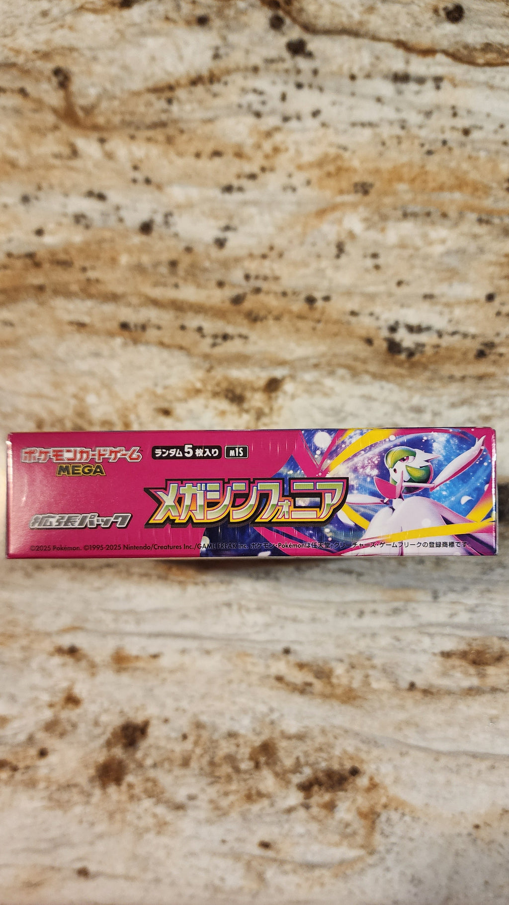 A rectangular box of Megadrive Mega Symphonia Japanese edition, featuring colorful anime graphics, placed on a textured beige stone surface.