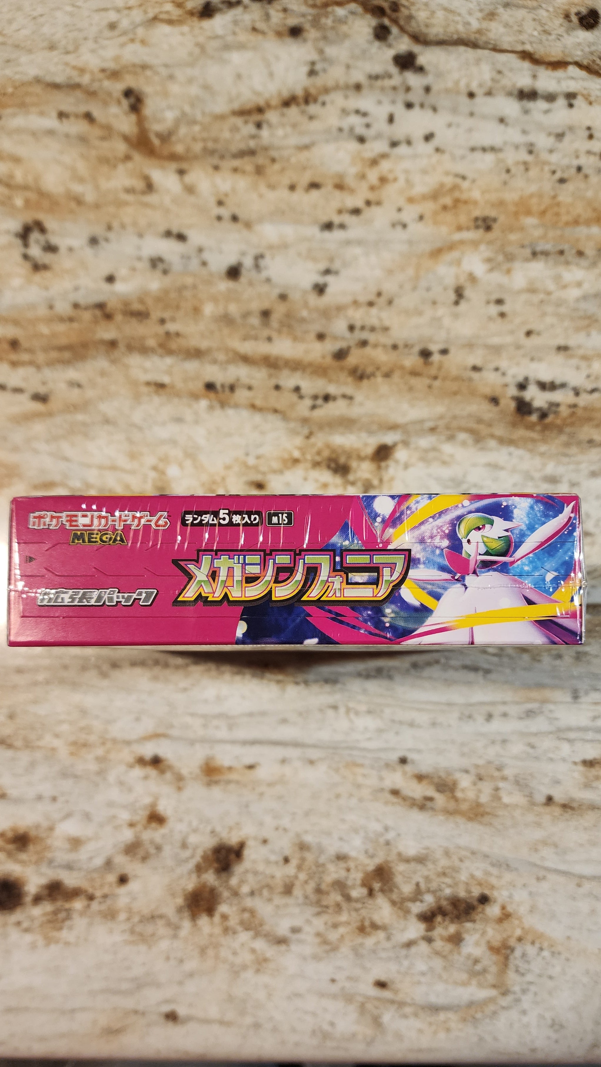 A Japanese box of Pokémon Mega Symphonia placed on a speckled beige stone surface.