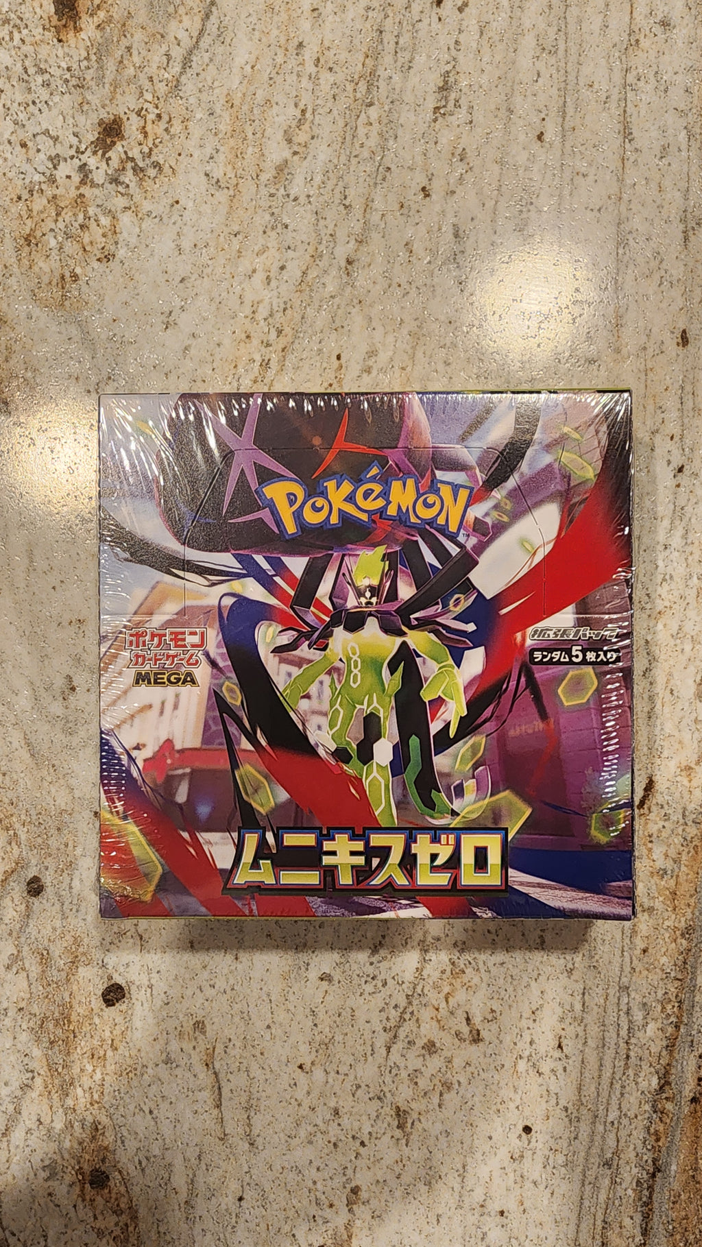 A sealed Pokémon trading card box featuring a colorful anime-style character illustration, photographed from above on a mottled stone-like surface.