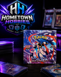 A sealed Pokémon TCG booster pack box stands on a dark tabletop, surrounded by cards in sleeves and a large Hometown Hobbies LLC logo in the background. The packaging artwork shows a stylized character with blue, red, and purple effects against a dark illustrated city scene.