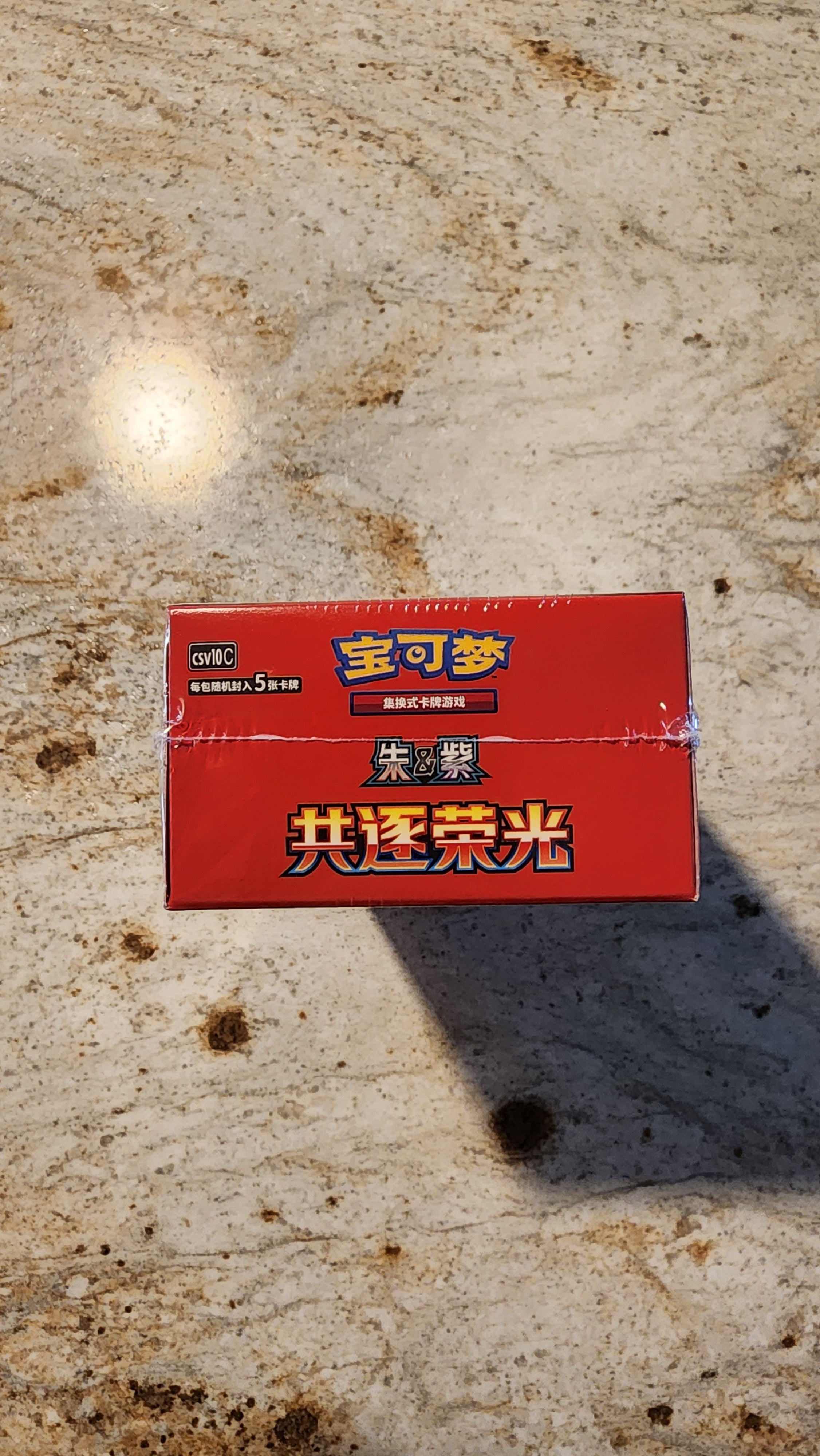 A red rectangular box of Chinese cigarettes with gold and white text, placed on a beige stone surface with a visible shadow.