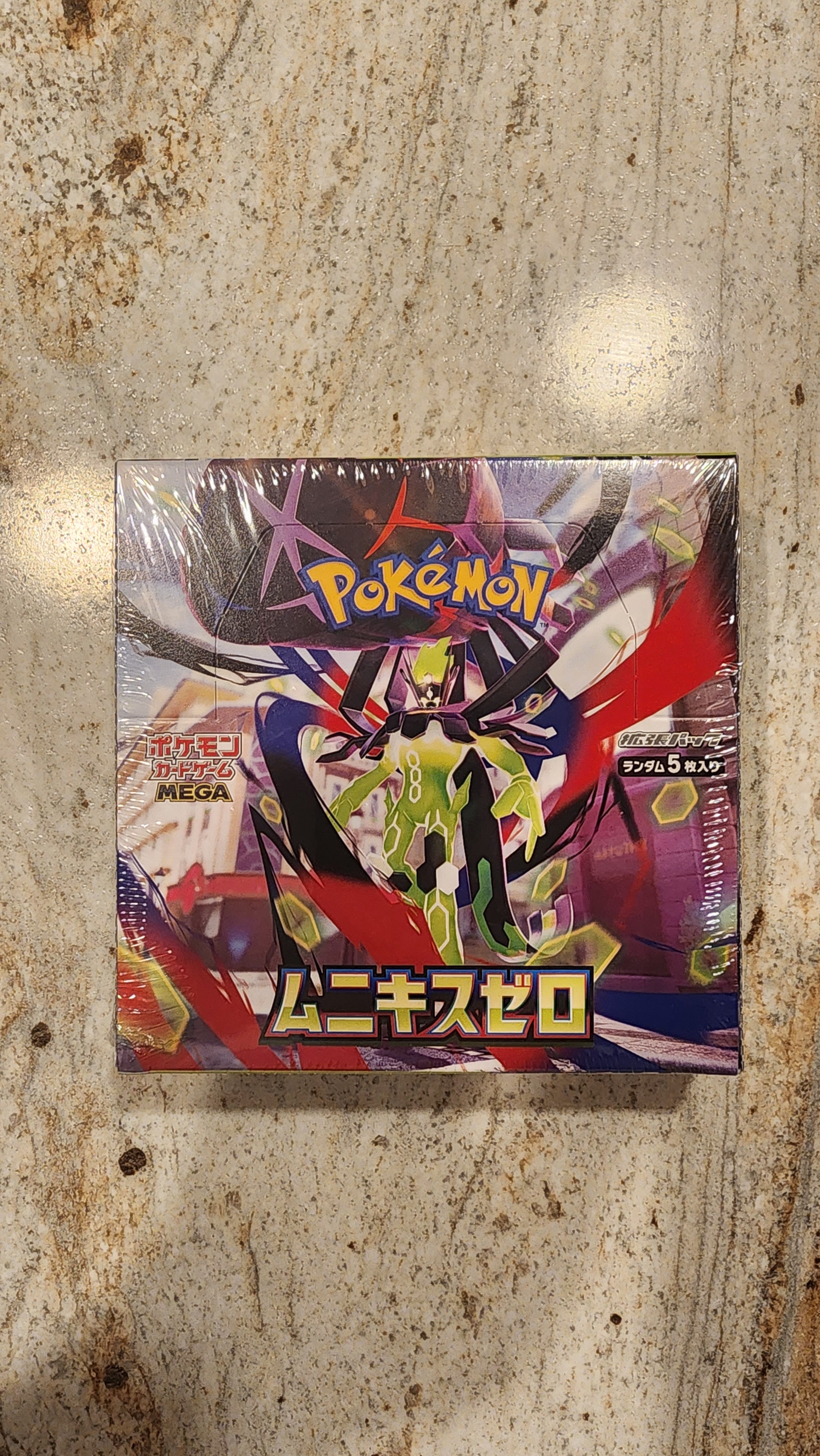 A sealed Pokémon trading card box featuring a colorful anime-style character illustration, photographed from above on a mottled stone-like surface.