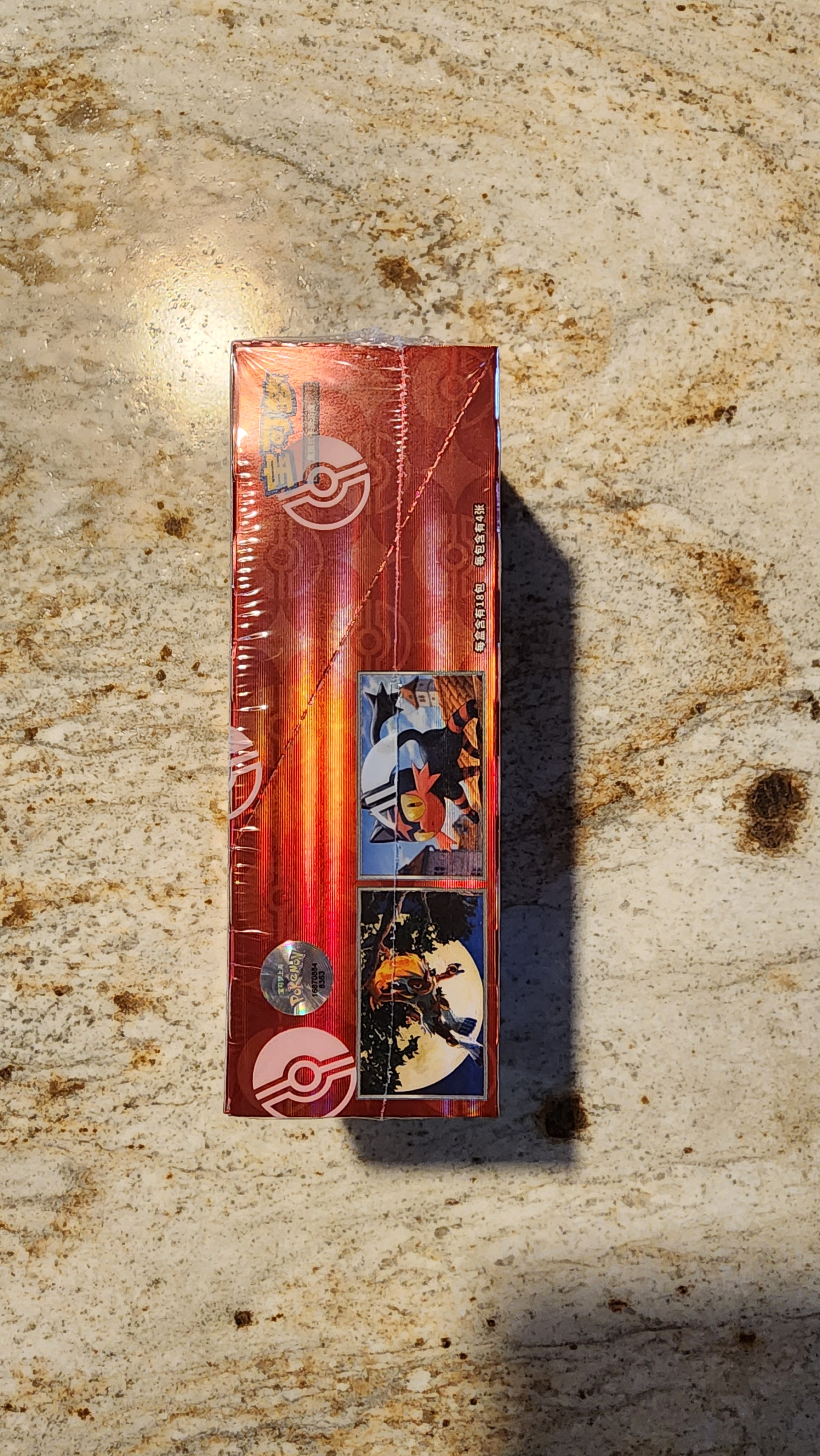A sealed red Pokéball trading card booster pack standing upright on a textured beige stone surface, with a strong shadow cast to the right.