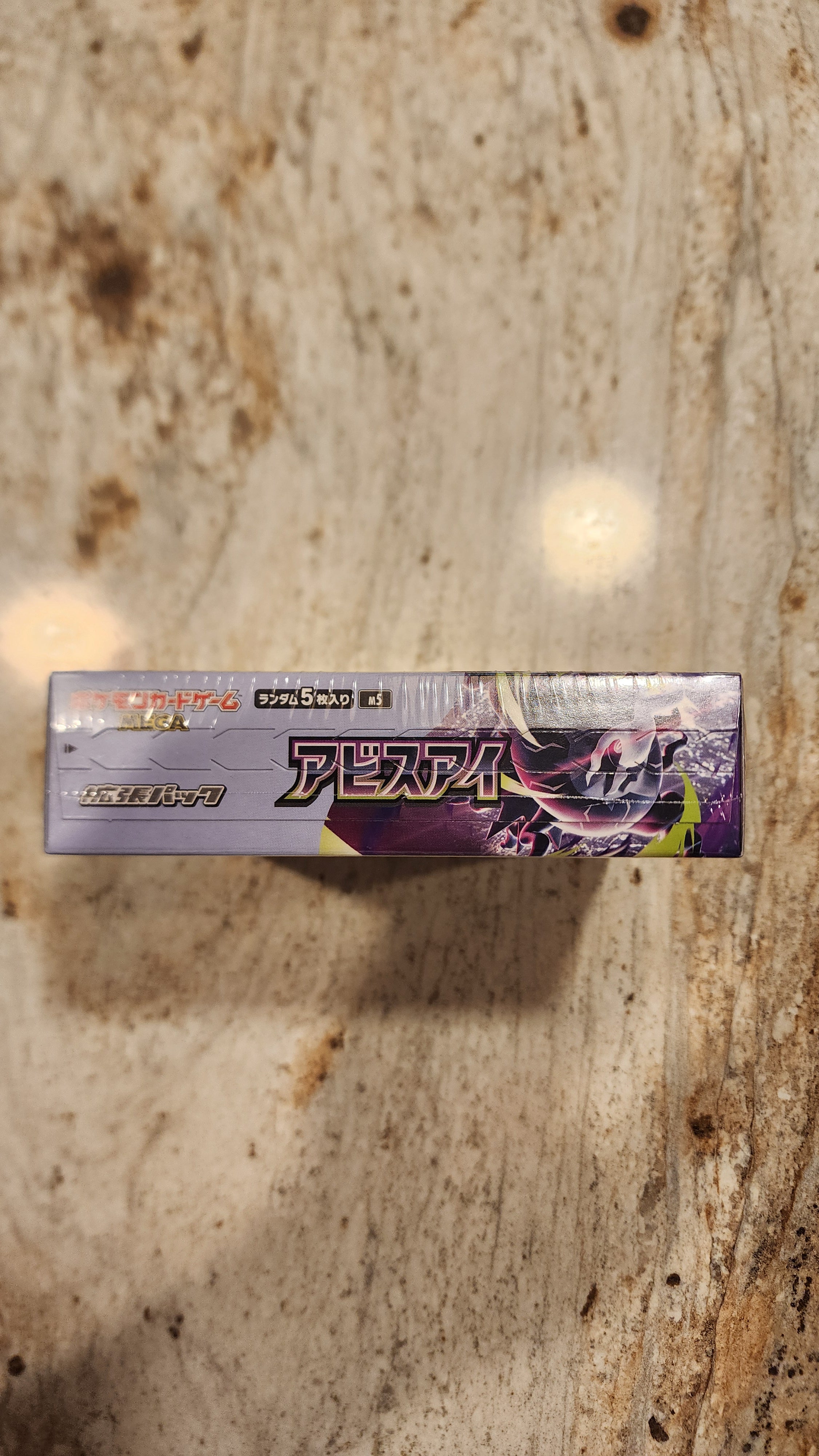 A sealed Japanese Pokémon Tens card pack standing vertically on a textured stone surface.